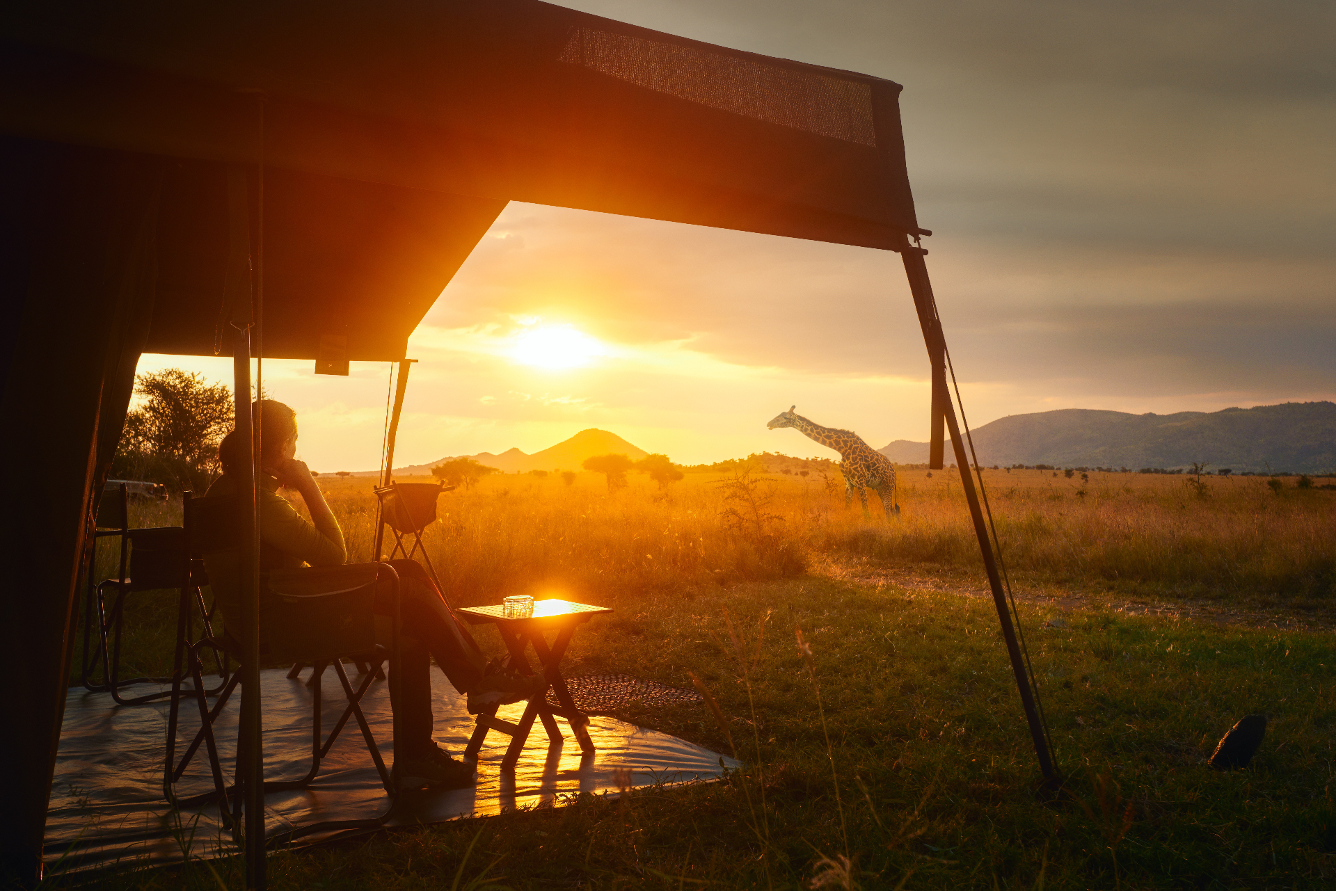 Tented safari camp at sunset with a giraffe on the horizon